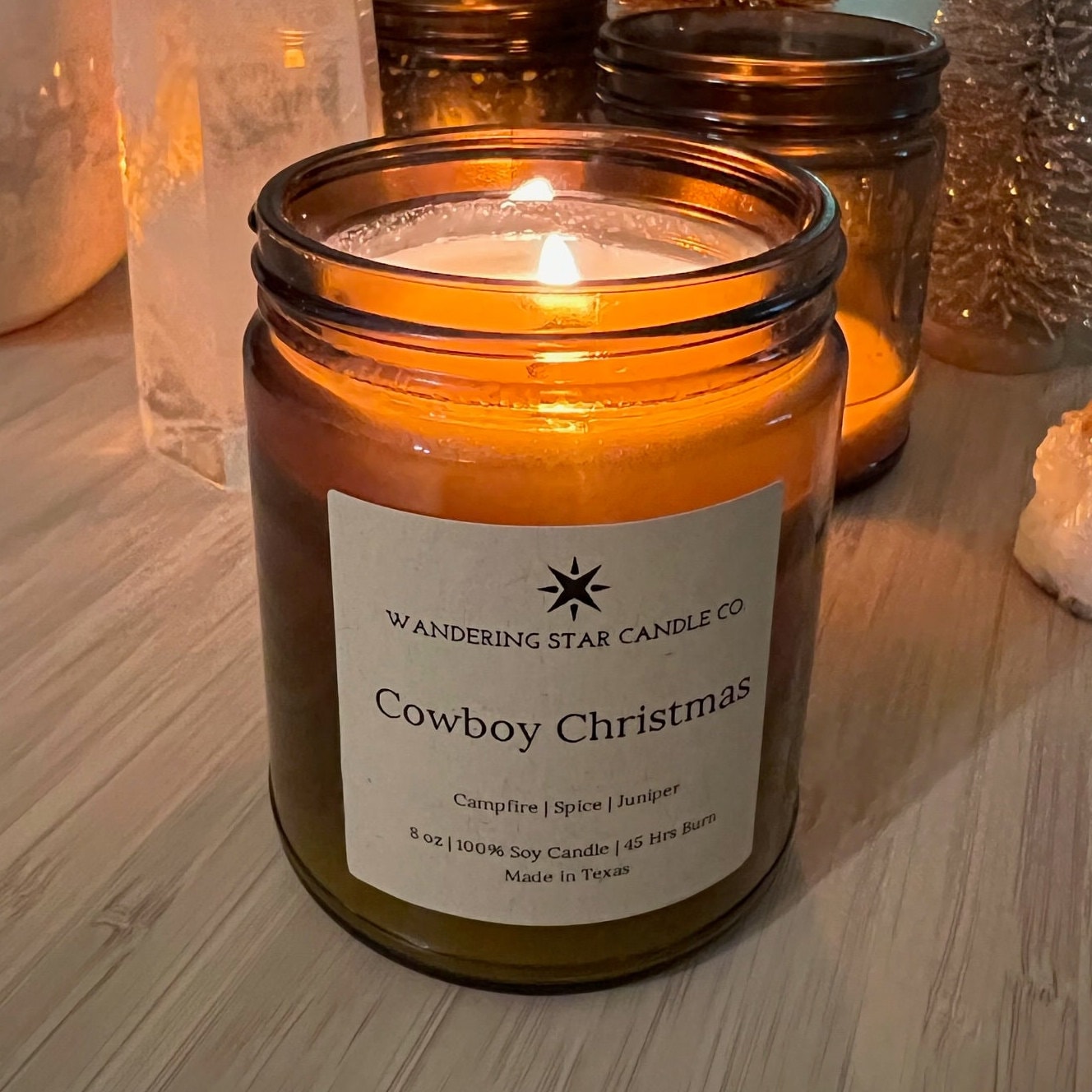 Photo of a lit amber jar candle featuring the scent of Cowboy Christmas, which is a blend of Campfire, Spice, and Juniper.