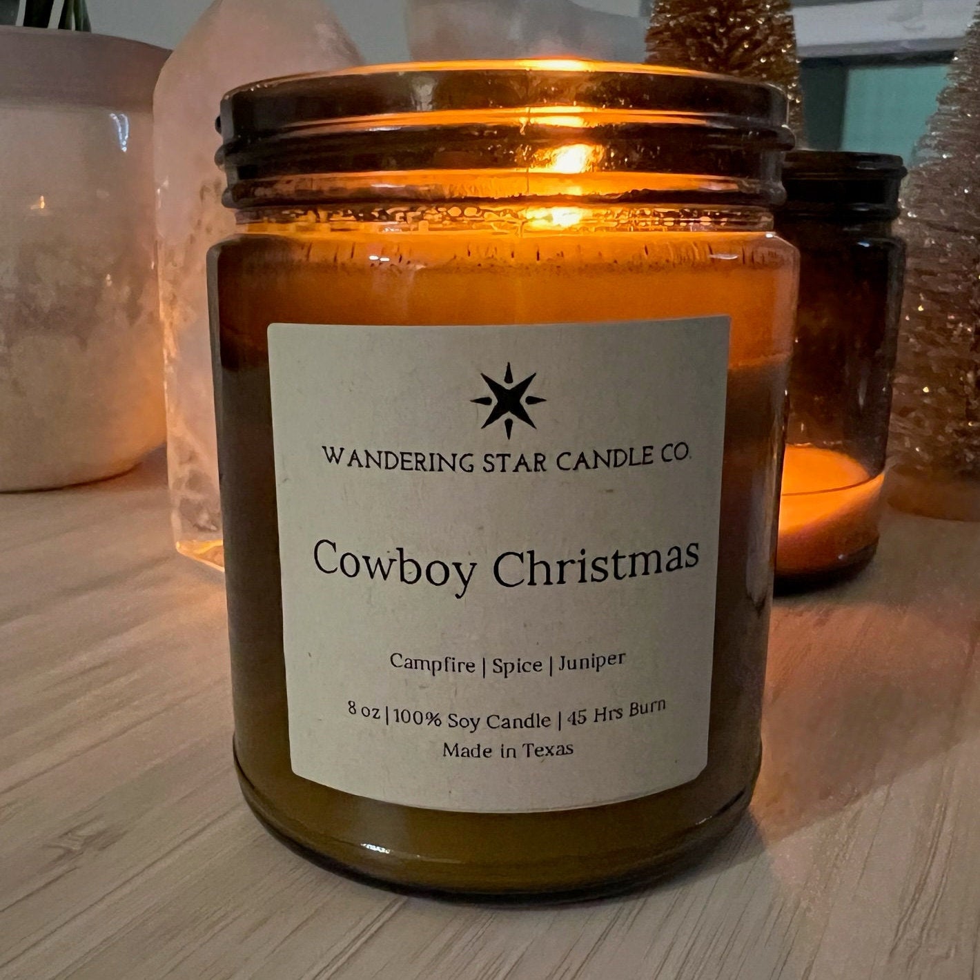 Photo of a lit amber jar candle featuring the scent of Cowboy Christmas, which is a blend of Campfire, Spice, and Juniper.