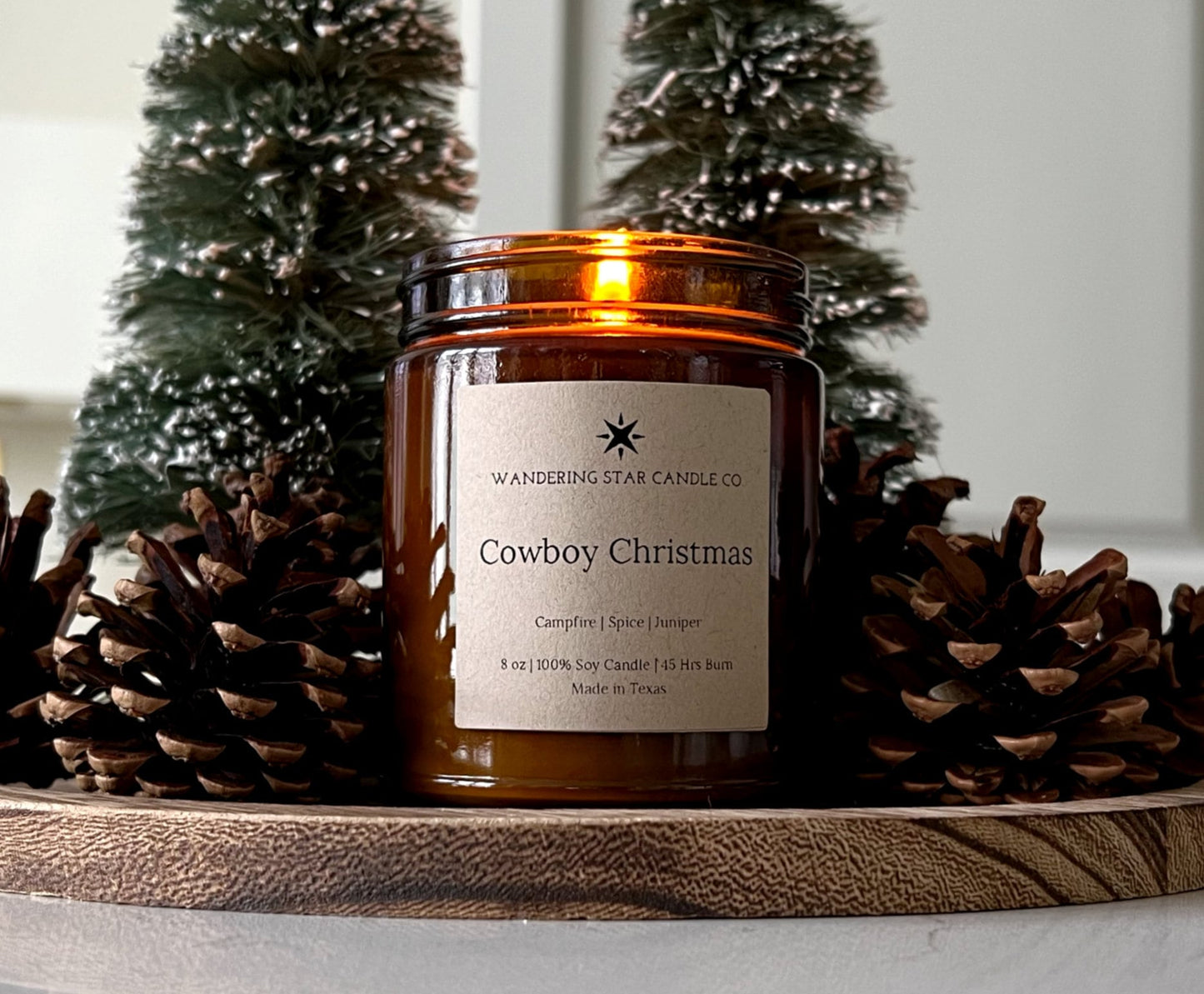 Photo of a lit amber jar candle featuring the scent of Cowboy Christmas, which is a blend of Campfire, Spice, and Juniper.